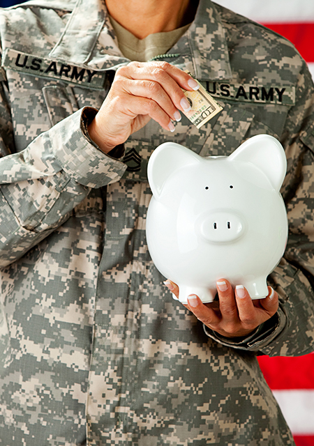 Soldier in uniform putting money into a white piggy bank